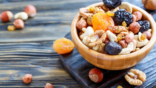 Bowl with a mixture of dried fruit and nuts on an old kitchen table, selective focus.