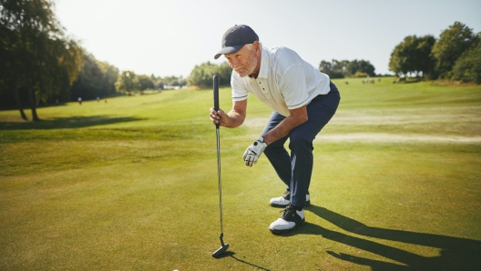 Sporty senior man crouching on a green planning his putt while enjoying a round of golf on a sunny day