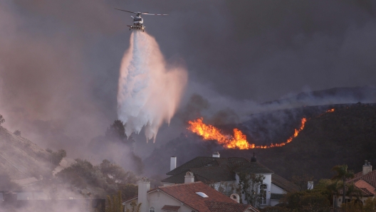 TOPSHOT - A helicopter drops water around homes threatened by the wind-driven Palisades Fire in Pacific Palisades, California, January 7, 2025. A fast-moving brushfire in a Los Angeles suburb burned buildings and sparked evacuations Tuesday as "life threatening" winds whipped the region. More than 200 acres (80 hectares) was burning in Pacific Palisades, a upscale spot with multi-million dollar homes in the Santa Monica Mountains, shuttering a key highway and blanketing the area with thick smoke. (Photo by David Swanson / AFP)