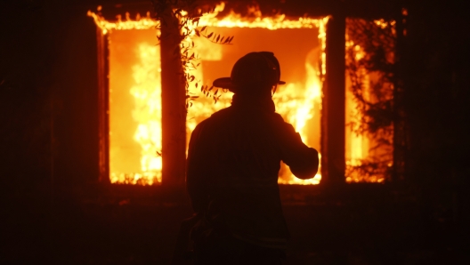 A firefighter is silhouetted in front of a burning structure as the Palisades Fire sweeps through in the Pacific Palisades neighborhood of Los Angeles, Tuesday, Jan. 7, 2025. (AP Photo/Etienne Laurent)