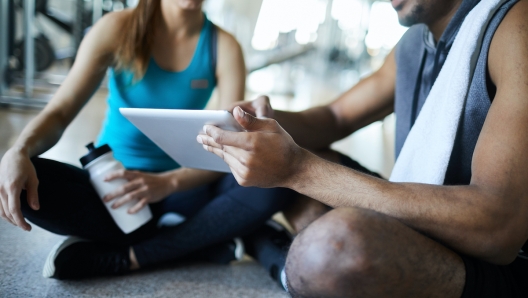 African-american guy in activewear and girl watching curious online stuff in touchpad while having break in gym