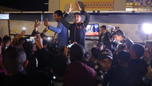 People celebrate while watching a television along a street in Khan Yunis in the southern Gaza Strip on January 15, 2025, amid the ongoing war in the Palestinian territory between Israel and Hamas. Thousands of Gazans celebrated on January 15 as news spread that a ceasefire and hostage release deal had been reached between Israel and Hamas, aimed at ending more than 15 months of war in the Palestinian territory. (Photo by BASHAR TALEB / AFP)