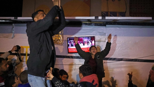 People celebrate while watching a television along a street in Khan Yunis in the southern Gaza Strip on January 15, 2025, amid the ongoing war in the Palestinian territory between Israel and Hamas. Thousands of Gazans celebrated on January 15 as news spread that a ceasefire and hostage release deal had been reached between Israel and Hamas, aimed at ending more than 15 months of war in the Palestinian territory. (Photo by BASHAR TALEB / AFP)