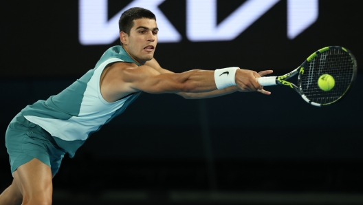 MELBOURNE, AUSTRALIA - JANUARY 21: Carlos Alcaraz of Spain stretches to play a backhand against Novak Djokovic of Serbia in the Men's Singles Quarterfinal match during day 10 of the 2025 Australian Open at Melbourne Park on January 21, 2025 in Melbourne, Australia. (Photo by Clive Brunskill/Getty Images)