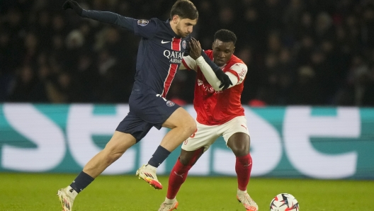 PSG's Khvicha Kvaratskhelia, left, is challenged by Reims' Aurelio Buta during the French League One soccer match between Paris Saint-Germain and Reims at Parc des Princes stadium in Paris, Saturday, Jan. 25, 2025. (AP Photo/Michel Euler)