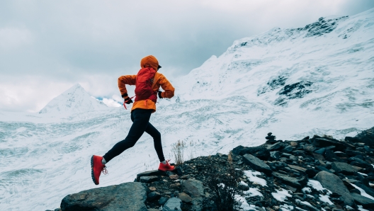 Woman trail runner cross country running up to winter snow mountain top