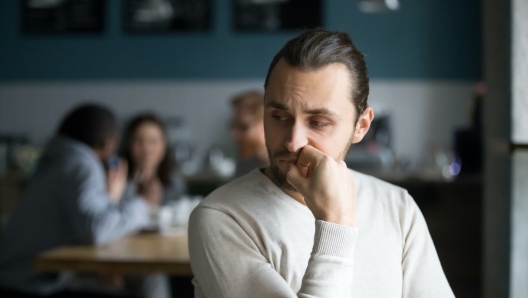 Upset millennial outsider feel offended lack company, young outcast guy suffer from discrimination, jealous of friends hang out together in caf, envious male loner depressed sit alone in coffeeshop