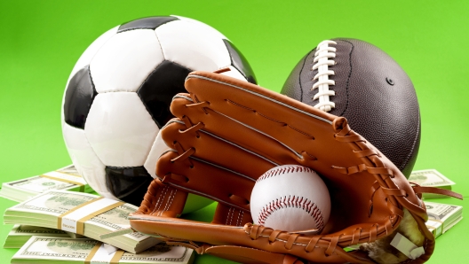 Winning bet on sporting event, money in sport and sports betting conceptual idea with baseball glove, football, soccer ball and wad of cash isolated on green background