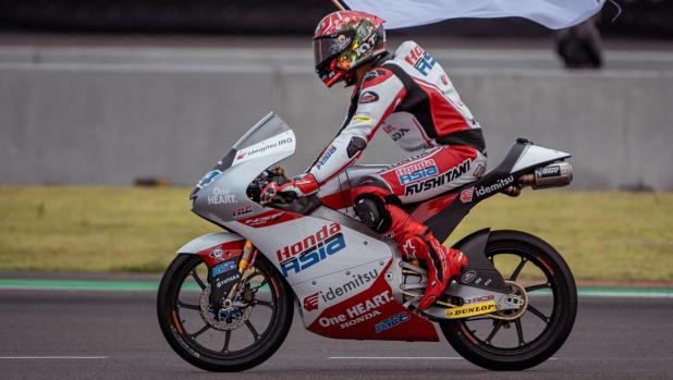 Honda Team Asia Indonesian rider Mario Aji carries the Indonesian flag after finishing the Indonesian Grand Prix Moto3 race at the Mandalika International Circuit at Kuta Mandalika in Central Lombok on March 20, 2022. (Photo by BAY ISMOYO / AFP)