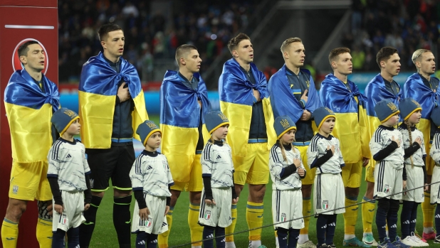 Ukraine players, drapped in their flag, line up for the national anthems prior to the UEFA EURO 2024 Group C qualifying football match between Ukraine and Italy at the BayArena Stadium in Leverkusen, western Germany on November 20, 2023. (Photo by LEON KUEGELER / AFP)