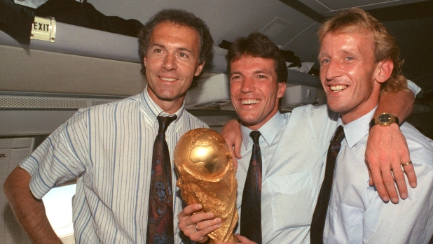 FILED - 09 July 1990, Italy, Rom: On the plane returning from Rome to Frankfurt, former DFB team manager Franz Beckenbauer (l), captain and midfielder Lothar Matthäus (M) and defender Andreas Brehme, who scored the decisive goal, present the World Cup trophy. Franz Beckenbauer is dead. The German soccer legend died on Sunday at the age of 78, his family told the German Press Agency on Monday. Photo: Wolfgang Eilmes/dpa (Photo by WOLFGANG EILMES / DPA / dpa Picture-Alliance via AFP)