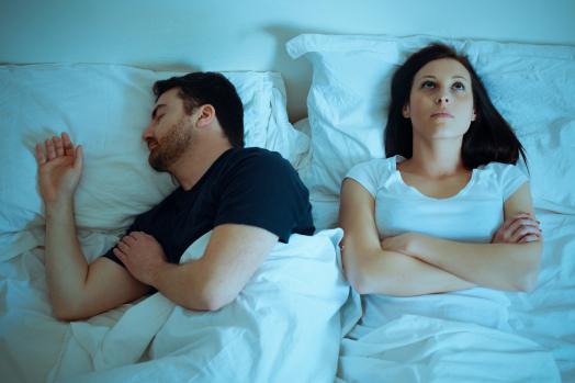 Sad and thoughtful woman awake while husband is sleeping in the bed