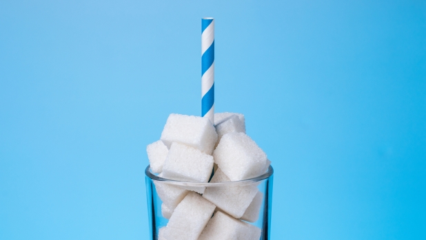 A glass with a straw is filled with pieces of sugar. Too much sugar in drinks, concept.