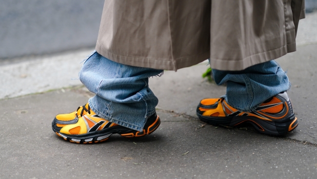 PARIS, FRANCE - JANUARY 15: A guest wears a long beige trench coat, blue denim jean pants, black and orange Luisaviaroma Spike Runner 2 sneaker, outside Berluti, during Paris Fashion Week - Menswear F/W 2020-2021 on January 17, 2020 in Paris, France. (Photo by Edward Berthelot/Getty Images)