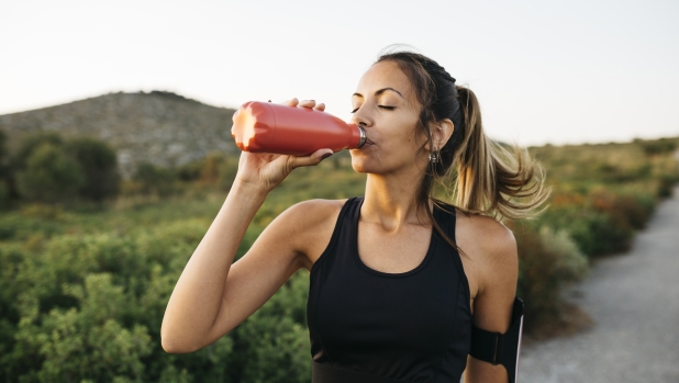 Fit young Woman in black sportswear drinking water from a reusable metal bottle after running workout