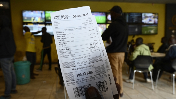 A sports enthusiast holds a betting slip while different games are broadcast on screens at a sports betting shop in July 15, 2019 in Nairobi. Kenya's Betting Control and Licence Board announced sweeping restrictions in May 2019, on gambling advertisements, including outright bans on celebrity endorsements and social media promotions, in a blow to the fast-growing gambling industry in East Africa. (Photo by SIMON MAINA / AFP)