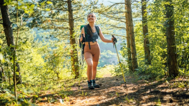 Young cheerful woman with climbing poles crossing mountain forest strea