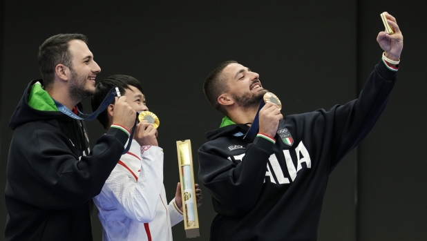 Bronze medalist Italy's Paolo Monna, right, uses his phone to take a selfie with gold medalist China's Xie Yu, center, and silver medalist and fellow countryman Frederico Nilo Maldini after the 10m air pistol men's final at the 2024 Summer Olympics, Sunday, July 28, 2024, in Chateauroux, France. (AP Photo/Manish Swarup)