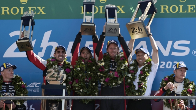 Sebastien Buemi of Switzerland, left, Brendon Hartley of New Zealand, center right, and Ryo Hirakawa of Japan, center left, hold their trophies after winning the 24-Hour Le Mans endurance race in their Toyota Gazoo Racing GRO10 Hybrid in Le Mans, western France, Sunday June 12, 2022. (AP Photo/Jeremias Gonzalez)