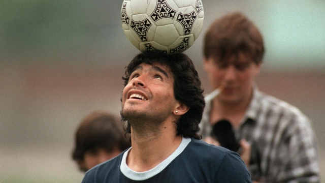 Argentine soccer star Diego Maradona, wearing a diamond earring, balances a soccer ball on his head as he walks off the practice field following the national selection's 22 May 1986 practice session in Mexico City. (Photo credit should read JORGE DURAN/AFP via Getty Images)