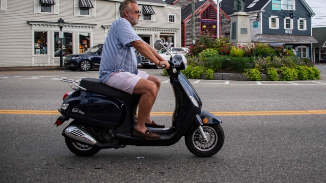 A man rides a Wolf Lucky scooter through the streets in Kennebunkport, Maine on July 22, 2022. - Weather in New England reached into the 90s (F) today and forecast call for temperatures to be close to 100 degrees (F) over the weekend. (Photo by Joseph Prezioso / AFP)