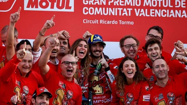 Ducati Italian rider Francesco Bagnaia (C) and his partner Domizia Castagnini (C-L) celebrate with team members after winning the MotoGP Valencia Grand Prix at the Ricardo Tormo racetrack in Cheste, on November 26, 2023. Italy's Francesco Bagnaia enjoyed a dream day as he retained his MotoGP world title and crowned it with victory in the final race of the season in Valencia today. The 26-year-old Ducati rider had been assured of the championship when his sole rival Jorge Martin crashed early in the race. (Photo by JOSE JORDAN / AFP)