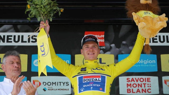 Team Soudal's Belgian rider Remco Evenepoel wearing the overall leader's yellow jersey celebrates on the podium after winning the fourth stage of the 76th edition of the Criterium du Dauphine cycling race, 34,4km individual time trial between Saint-Germain-Laval and Neulise, central France, on June 5, 2024. (Photo by Thomas SAMSON / AFP)