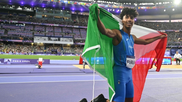 Bronze medallist Italy's Mattia Furlani celebrates with the natrional flag after competing in the men's long jump final of the athletics event at the Paris 2024 Olympic Games at Stade de France in Saint-Denis, north of Paris, on August 6, 2024. (Photo by Andrej ISAKOVIC / AFP)