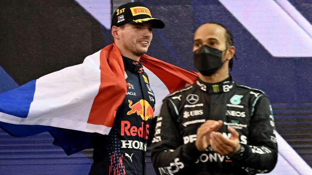TOPSHOT - 2021 FIA Formula One World Champion Red Bull's Dutch driver Max Verstappen walks past second-placed Mercedes' British driver Lewis Hamilton (R) on the podium of the Yas Marina Circuit after the Abu Dhabi Formula One Grand Prix on December 12, 2021. - Max Verstappen became the first Dutchman ever to win the Formula One world championship title when he won a dramatic season-ending Abu Dhabi Grand Prix at the Yas Marina circuit on December 12, 2021. The Red Bull driver won his 10th race of the season to finish ahead of seven-time champion Lewis Hamilton. (Photo by ANDREJ ISAKOVIC / AFP)