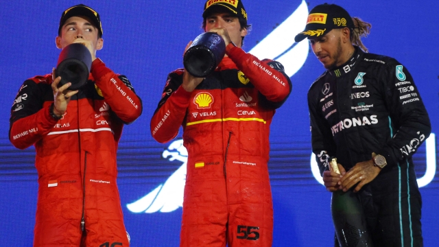 Winner Ferrari's Monegasque driver Charles Leclerc (L) celebrate on the podium second place Ferrari's Spanish driver Carlos Sainz Jr  and third placed Mercedes' British driver Lewis Hamilton (R) after the Bahrain Formula One Grand Prix at the Bahrain International Circuit in the city of Sakhir on March 20, 2022. (Photo by Giuseppe CACACE / AFP)