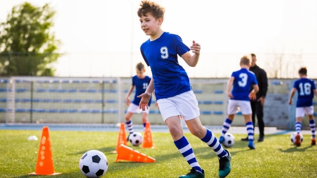Kids Sports: Teaching Children to Improve Soccer Skills. Football camp for kids. Boys practice dribbling in field. Players develop skills. Children training with balls and cones. Soccer slalom drills