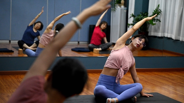 This photo taken on July 30, 2022 shows yoga instructor Feng (R) stretching with students at a gym in Beijing's middle-class neighbourhood of Shangdi. - It is 10 years since Xi unveiled the "Chinese Dream", a grand vision to restore the country's global influence through a collective struggle for prosperity, power and glory, steered by the Chinese Communist Party. (Photo by NOEL CELIS / AFP) / TO GO WITH China-Xi-congress-economy-politics, SPECIAL REPORT by Matthew WALSH