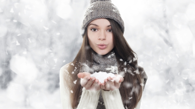 Winter portrait. Young, beautiful woman blowing snow toward camera on winter background