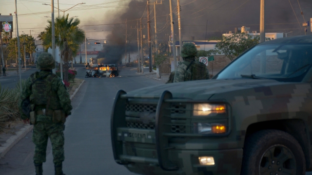 TOPSHOT - Mexicans soldiers stand guard near burning vehicles on a street during an operation to arrest the son of Joaquin "El Chapo" Guzman, Ovidio Guzman, in Culiacan, Sinaloa state, Mexico, on January 5, 2023. - Mexican security forces on Thursday captured a son of jailed drug kingpin Joaquin "El Chapo" Guzman, scoring a high-profile win in the fight against powerful cartels days before US President Joe Biden visits. Ovidio Guzman, who was arrested in the northwestern city of Culiacan, is accused of leading a faction of his father's notorious Sinaloa cartel, Defense Minister Luis Cresencio Sandoval told reporters. (Photo by Juan Carlos CRUZ / AFP)