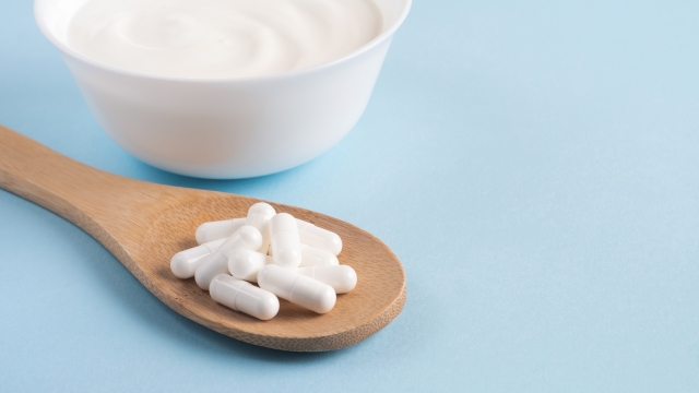 Homemade yogurt with probiotics and capsules pills on a wooden spoon. Close up, copy space