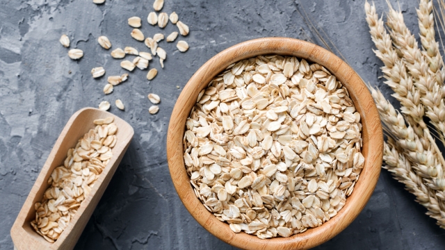 Rolled oats or oat flakes in wooden bowl and golden wheat ears on stone background. Top view, horizontal. Healthy lifestyle, healthy eating, vegan food concept
