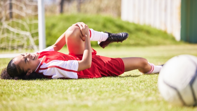 injured, pain or injury of a female soccer player lying on a field holding her knee during a match. Hurt woman footballer  with a painful leg on the ground in agony having a bad day on the pitch