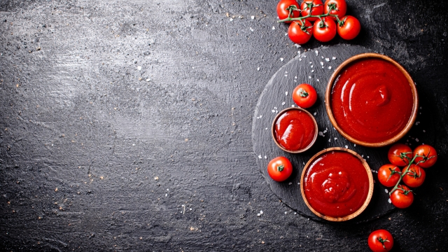 Tomato sauce in a wooden plate on a stone board with salt. On a black background. High quality photo
