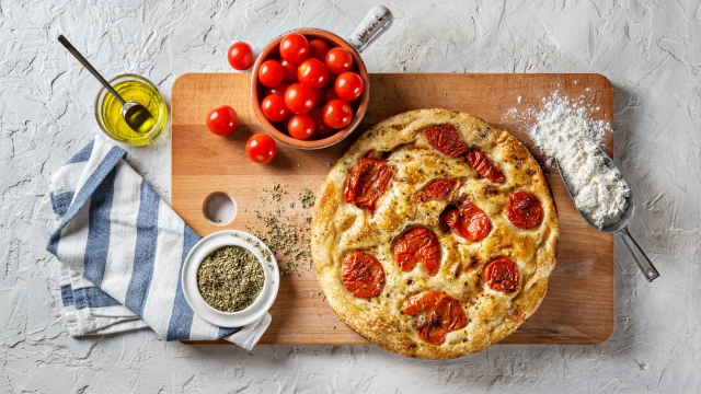 Bari-style focaccia bread. Focaccia barese with cherry tomatoes, olive oil and oregano on white plaster background, top view.