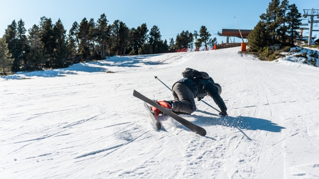 An adult boy dressed in ski clothes, is falling in the snow while skiing down a mountain ski slope, during the winter season.