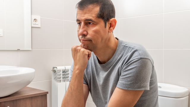 Shot of an bored and constipated man using the toilet at home