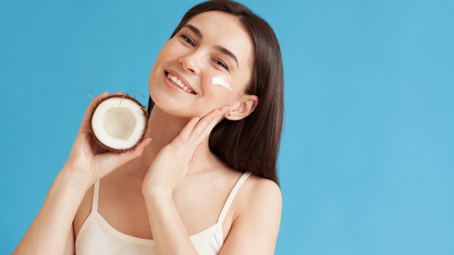 Lovely woman holding coconut and applying moisturizing cream on her face. Daily beauty routine