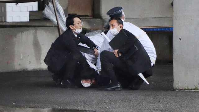 A man (bottom) is arrested after throwing what appeared to be a smoke bomb in Wakayama on April 15, 2023. - Japanese Prime Minister Fumio Kishida was evacuated from a port in Wakayama after a blast was heard, but he was unharmed in the incident, local media reported on April 15. (Photo by JIJI Press / AFP) / Japan OUT