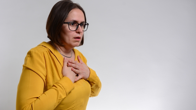 Pretty brunette woman having breath difficulties in front of white background. A young woman holding her breast in pain