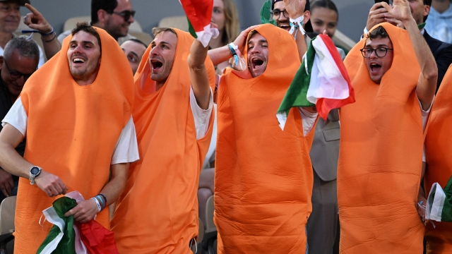 Fans of Italy's Jannik Sinner, dressed as carrots, gestures during his men's singles match against France's Alexandre Muller on day two of the Roland-Garros Open tennis tournament at the Court Philippe-Chatrier in Paris on May 29, 2023. (Photo by Emmanuel DUNAND / AFP)