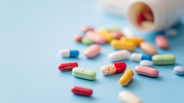 Colorful Pills scattered from white plastic medicine container on blue background. Shallow DOF