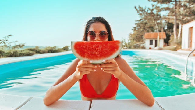 Beautiful, attractive woman enjoying in the pool, holding a watermelon
