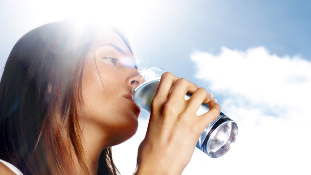 Young woman drinking a glass of water against the sunny sky