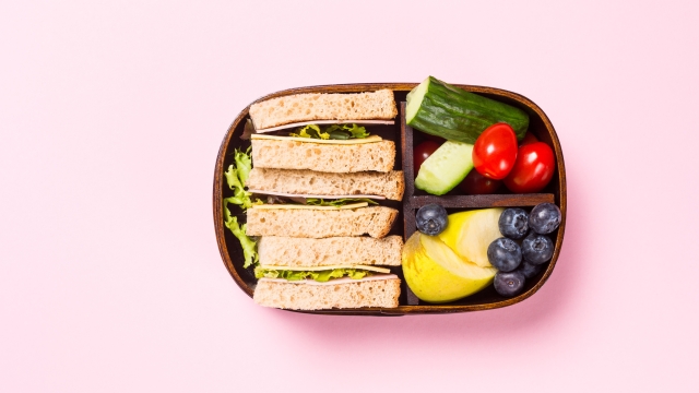 School wooden lunch box with sandwiches, vegetables, , tomatoes and fruits on pink background. Healthy children eating concept flat lay. Top view with copy space.