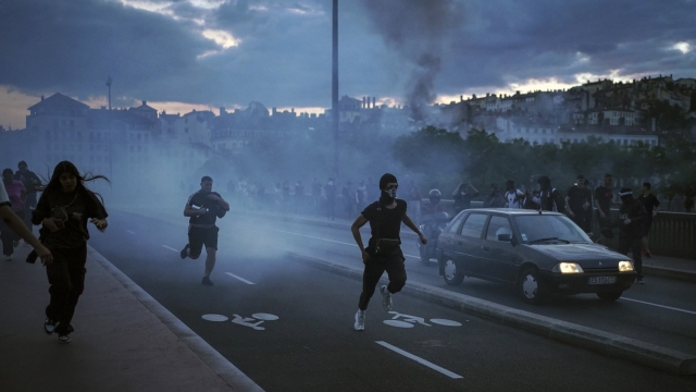 People run away during clashes with police in the center of Lyon, central France, Friday, June 30, 2023. French President Emmanuel Macron urged parents Friday to keep teenagers at home and proposed restrictions on social media to quell rioting spreading across France over the fatal police shooting of a 17-year-old driver. Writing on wall reads in French "Justice for Nahel" (AP Photo/Laurent Cipriani)